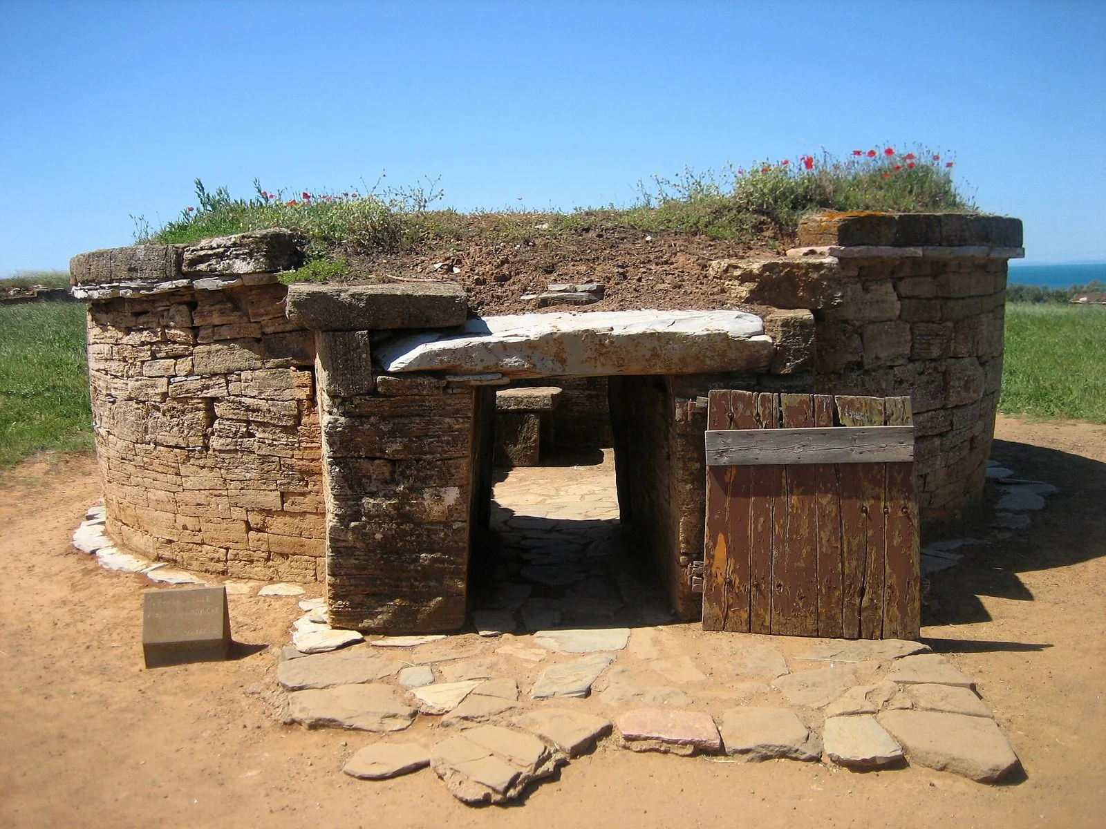 Tomba etrusca a tumulo in pietra con ingresso a corridoio e porta di legno nella necropoli di San Cerbone a Populonia, con il mare sullo sfondo