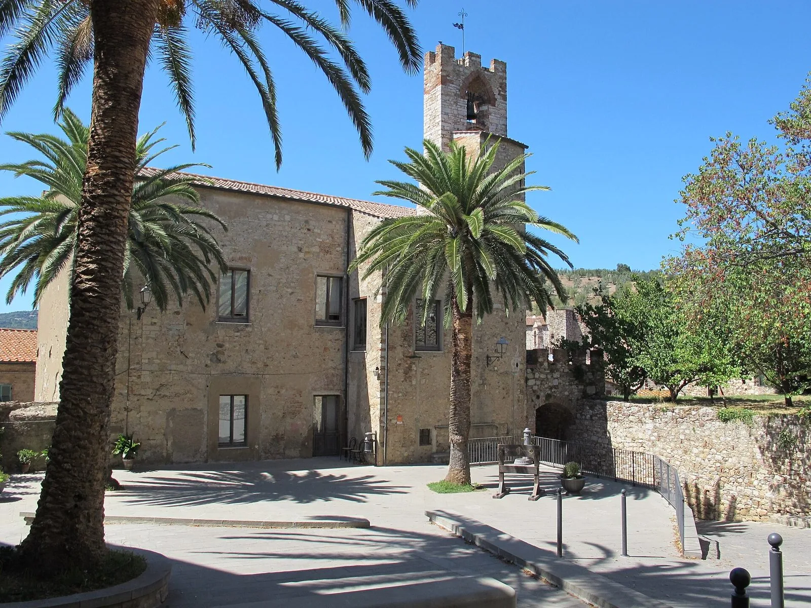 Il Palazzo Comunale di Suvereto in pietra con la torre campanaria merlata, incorniciato da due palme in una piazza soleggiata
