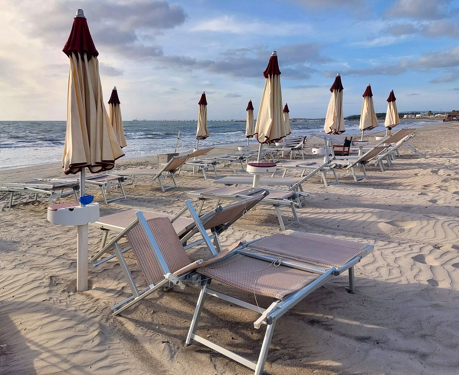 Ombrelloni chiusi e lettini sulla spiaggia di Vada in una giornata ventosa d'autunno, con il mare mosso e il cielo nuvoloso