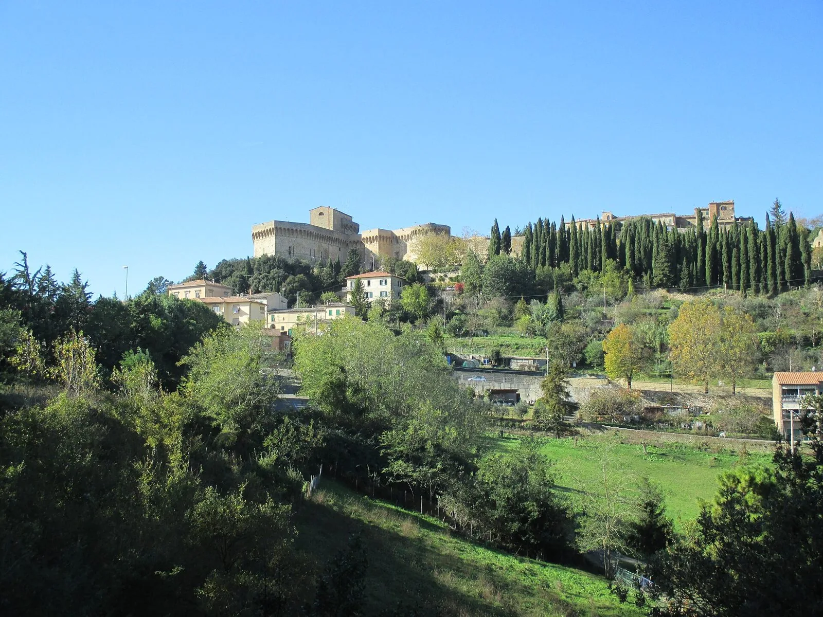 La Fortezza Medicea di Volterra in cima alla collina, tra cipressi e alberi, vista dalla campagna sottostante in una giornata di sole